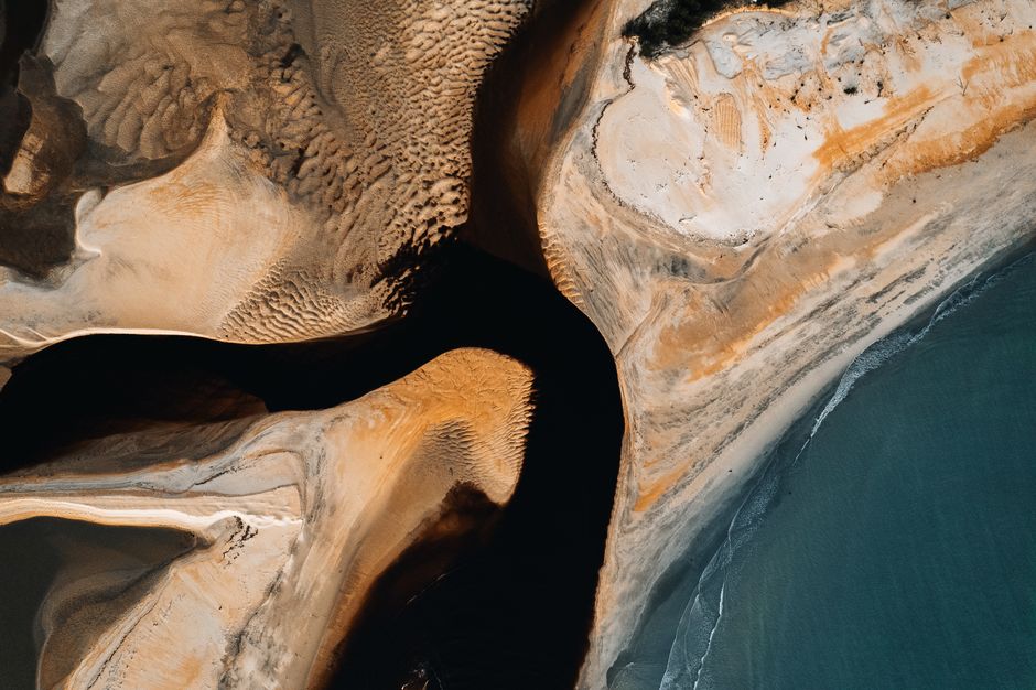 Aerial photography showcasing abstract sand formations meeting ocean shoreline.
