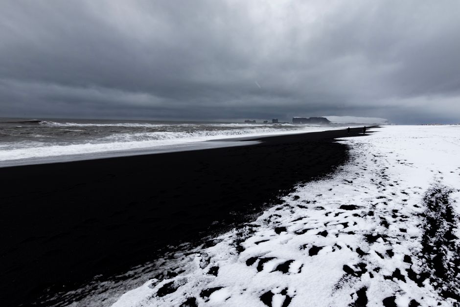 Stunning black sand beach with snow contrast under ominous clouds, captured in winter.